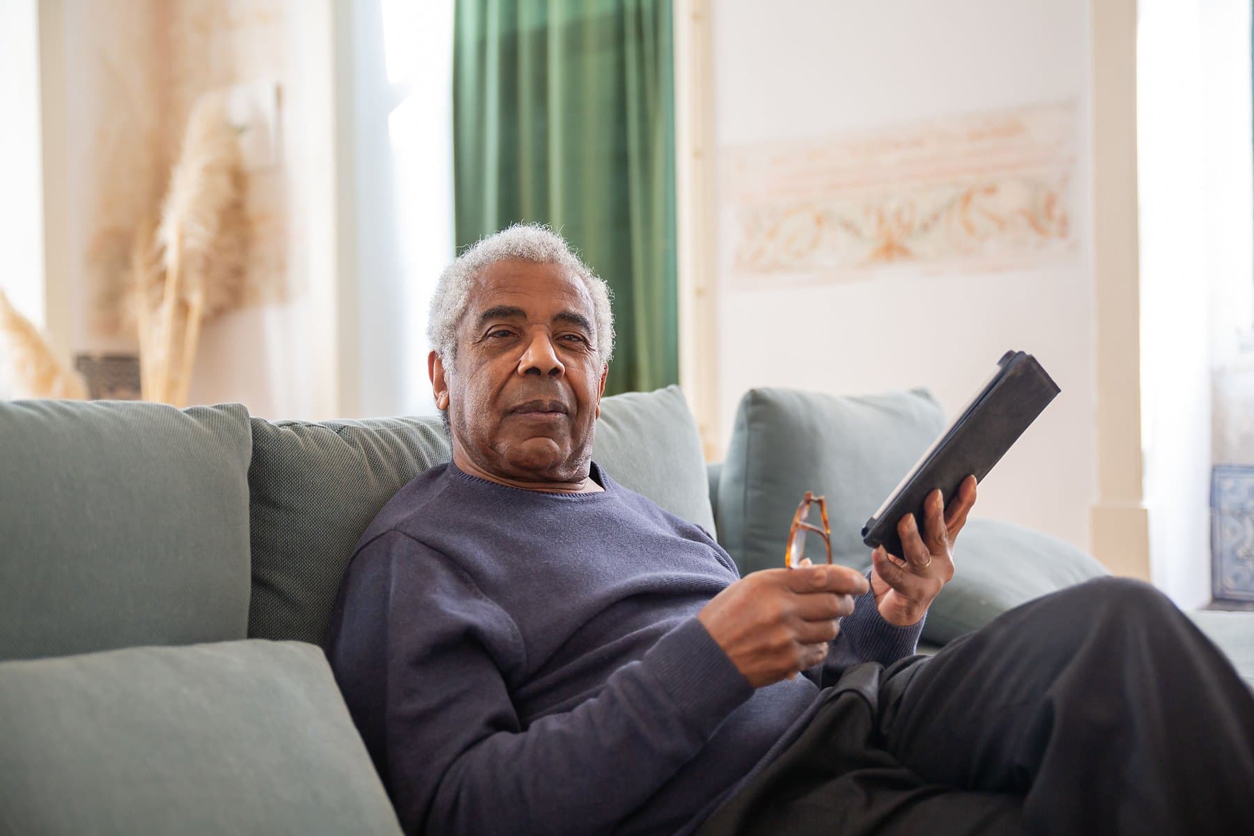 A senior man relaxing on a sofa at home while reading a tablet
